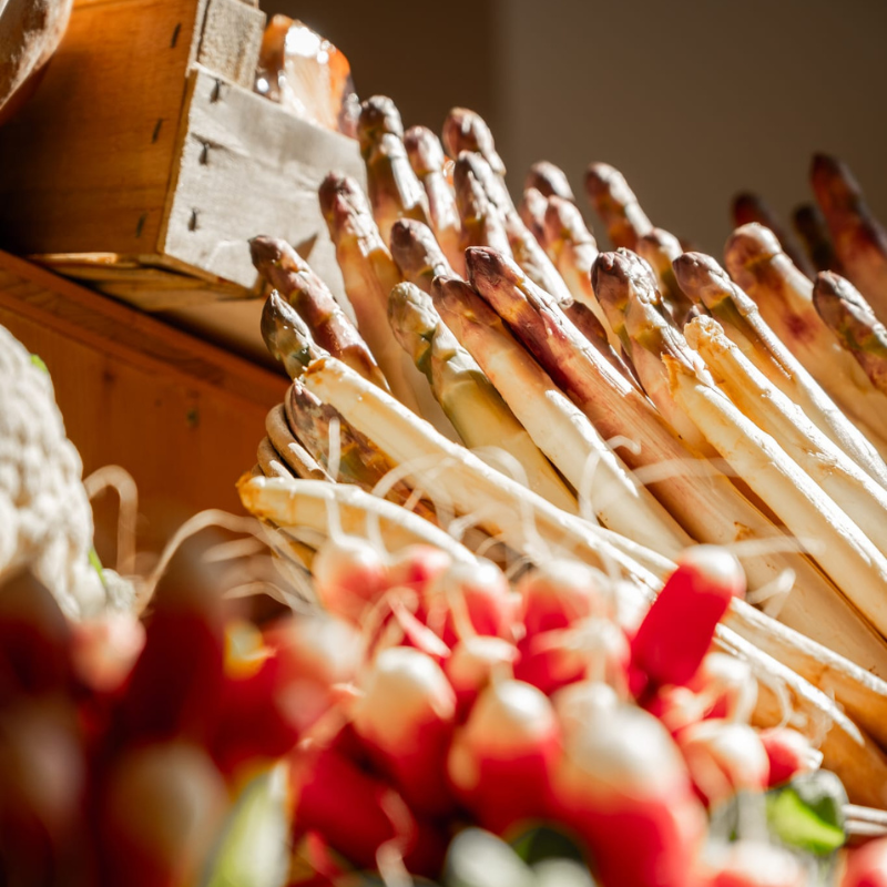 Rédaction-web-boutique-miam Bottes d'asperges blanches fraîches et radis rouges sur un étal de marché, mettant en valeur des légumes de saison locaux et savoureux